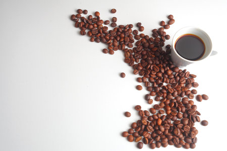 cup of hot coffee next to a spread of roasted coffee beans on a clean white background, highlighting...
