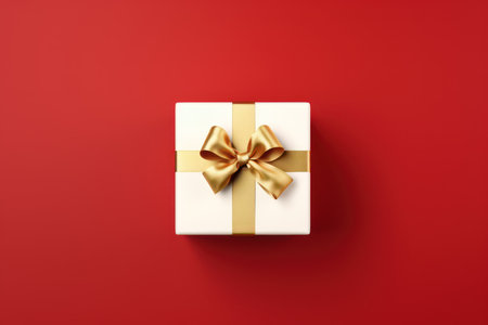White gift box with gold bow on red background. Top view.の素材