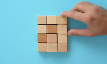 Hand carefully arranging wooden cubes into a staircase formation, symbolizing business growth and success, set against a clean blue background with ample copy space.の素材