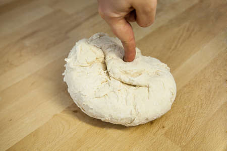Freshly kneaded hard unripened wheat dough on a wooden table with the hand on top. Preparation of...