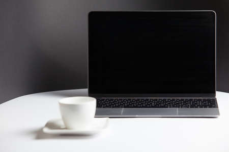 Composition with a modern opened laptop and coffee cup with saucer on the white table on a gray background. Remote workplace, home office. Moke up with laptop and coffe cup.の写真素材