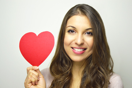 Valentine's Day. Beautiful young woman in love holding a paper heart and smile at camera on gray background.の写真素材