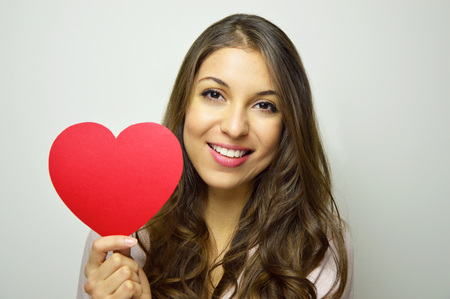 Valentine's Day. Beautiful young woman holding a paper heart and smile at camera on gray background.の写真素材