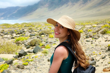Happy beautiful girl with straw hat looking at camera. Young female backpacker exploring Lanzarote,...