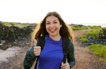 Happy hiking woman giving thumbs up. Young hiker woman smiling joyful at camera outdoor on hike trip. Beautiful young multiracial woman discovering Lanzarote Island.の写真素材