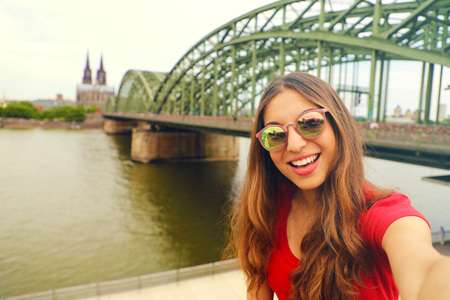 Selfie photo of young woman in Cologne with Hohenzollern Bridge and Cathedral on the background, Cologne, Germany. Traveling in Europe. Vintage Filter.の写真素材
