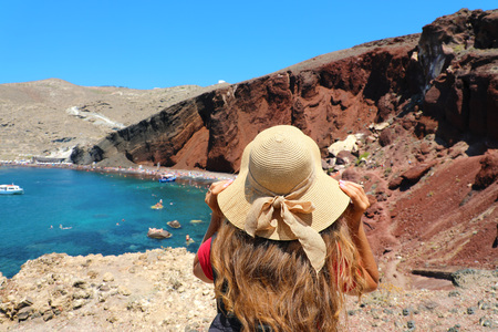 Woman holding her hat in the volcanic island of Santorini looking at the Red beach, Greece, Europeの写真素材