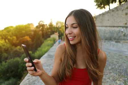 Happy beautiful woman send messages with application on the mobile phone outdoorの写真素材