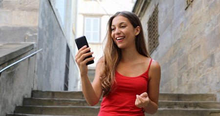 Front view of a fashion happy woman walking and using a smart phone on a old city street