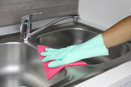 Hands in protective gloves with rag wiping sink. Maid or housewife cleans house. General cleaning or regular wash up.の写真素材