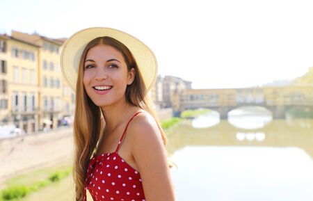 Happy smiling girl in Florence with Ponte Vecchio bridge and Arno river on the background. Portrait of young woman visiting Tuscany beauty in Italy.の写真素材