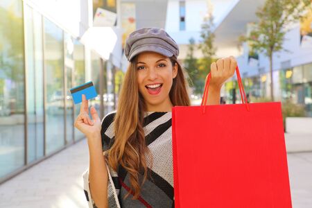 Happy smiling fashion woman holding shopping bag and credit card in her hands in a mall.