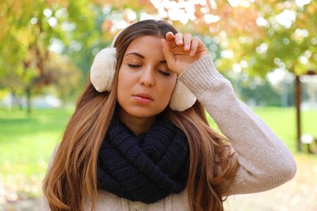 Girl with earmuffs suffering migraine headache fever outdoors.の写真素材
