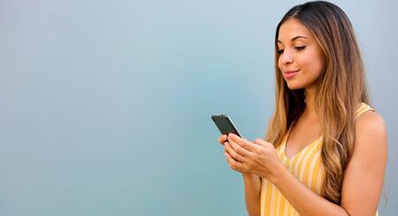 Brazilian woman typing on smart phone outdoor on gray background.