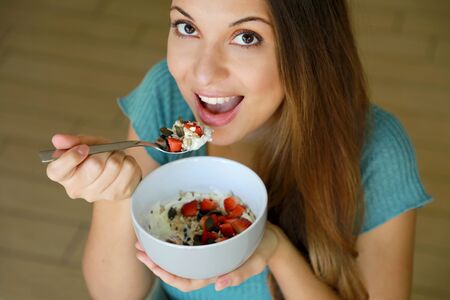 Close up view from above of beautiful young woman eating skyr with cereal muesli fruit and seeds at home, focus on model eyes indoor shot. Healthy food concept.の写真素材