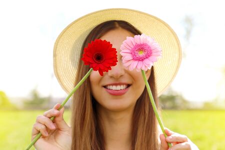 Young woman covering her eyes with fresh colorful flowers. Beautiful girl enjoying spring time. Focus on flowers.の写真素材