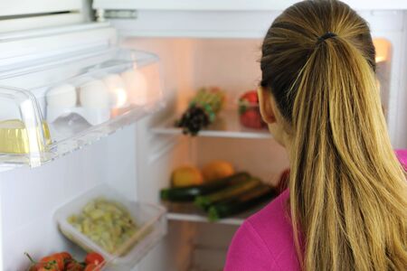 Back view of young woman looks inside the fridge searching for healthy foodの写真素材