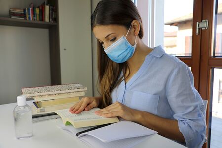 COVID-19 Pandemic Coronavirus Home Schooling Student Girl with Surgical Mask Studying from Home. Distance learning quarantine young woman reading and studying from home for virus disease 2019-nCoV.の写真素材