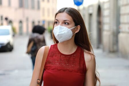 COVID-19 Young woman walking in city street wearing KN95 FFP2 mask protective for spreading of disease virus SARS-CoV-2. Girl with protective mask on face against Coronavirus Disease 2019.の写真素材