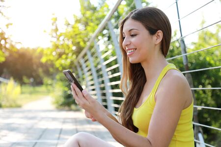 Beautiful sporty girl sitting in the park using smart phone app tracking performance after running workoutの写真素材