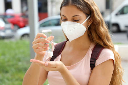 School girl wearing KN95 FFP2 mask using hand sanitizer in city streetの写真素材