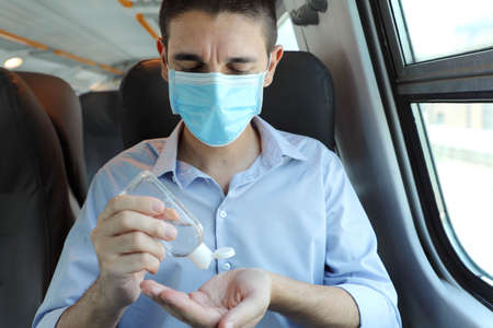 Travel safely on public transport. Business man with surgical mask using wash hand sanitizer gel dispenser. Passenger with protective mask disinfects hands on public transport.の写真素材