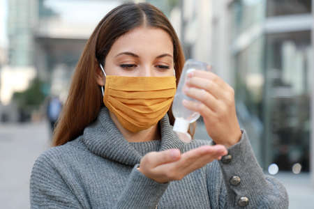Close up of young woman with protective mask using alcohol gel sanitizer hands in modern city streetの写真素材