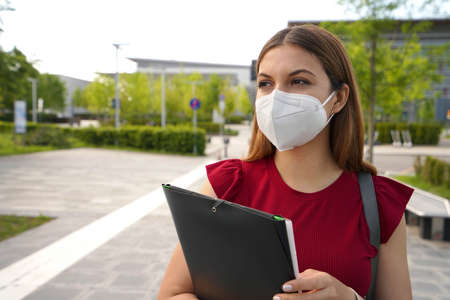 Portrait of beautiful girl with FFP2 KN95 face mask holding folders looking to the side outdoorsの写真素材