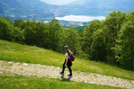 Female hiker walks the trail and looks with satisfaction from the top of mountain the lake