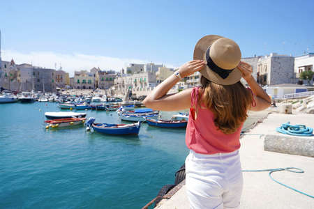 Holidays in Apulia. Back view of tourist girl wearing hat and looking at Giovinazzo picturesque harbor in Apulia, Italy.の写真素材