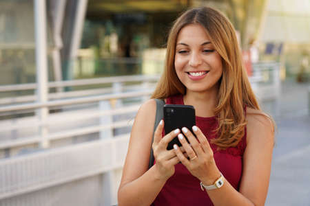 Brazilian girl using smartphone outdoor. Cheerful young woman chatting with mobile phone near train...