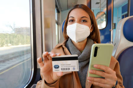 Happy confident woman with FFP2 KN95 protective mask traveling with train looking at camera holding credit card and smart phoneの写真素材