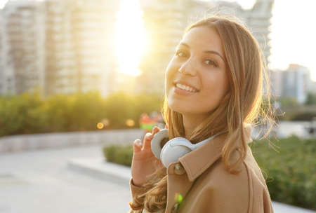 Young woman takes off her headphones and smiles on camera relaxing outdoor at sunsetの写真素材