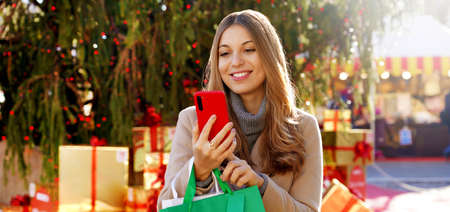 Fashion stylish woman receiving christmas wishes on smartphone when walking between christmas...