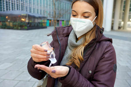 Woman with KN95 FFP2 mask using alcohol gel sanitizing her hands in city street