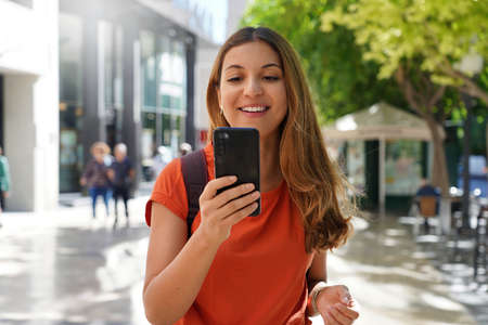 Portrait of happy young fashion woman watching at mobile phone in city