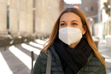 Young blonde woman wearing protective medical mask walking in the city with winter clothesの写真素材