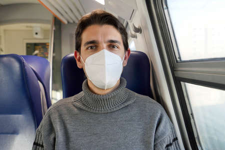 Close up of male commuter wearing FFP2 KN95 protective mask on train looking at camera