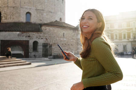 Beautiful smiling girl walking holding phone in Brescia, Italy