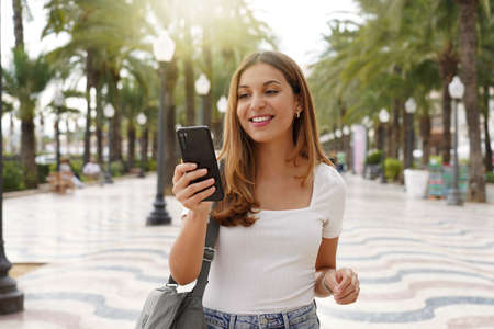 Traveler girl looking for hotel on cellphone. Smiling female tourist booking a room for the night...