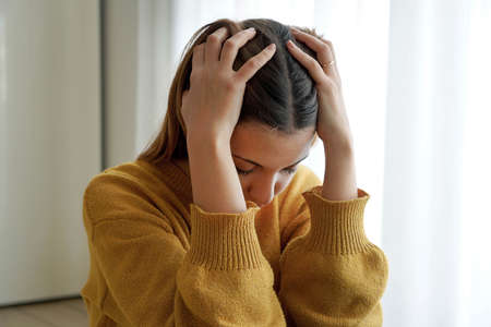 Mental health. Sad girl sitting on floor with hands in her hair frustrated.の写真素材