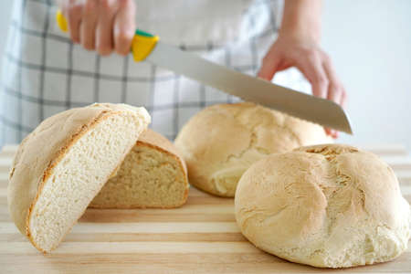 Woman cutting homemade bread on wooden table, close-up