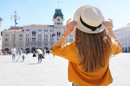 Tourism in Europe. Back view of pretty girl holding hat in Trieste, Italy. Beautiful young woman visiting Europe.の写真素材