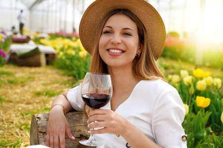 Relaxed beautiful woman enjoying a glass of red wine between tulips on spring timeの写真素材