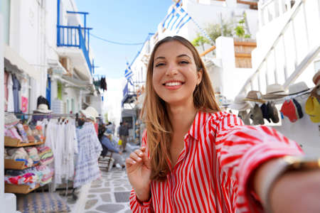 Self portrait of young cute traveler woman through the alleys in Mykonos picturesque town in Greece
