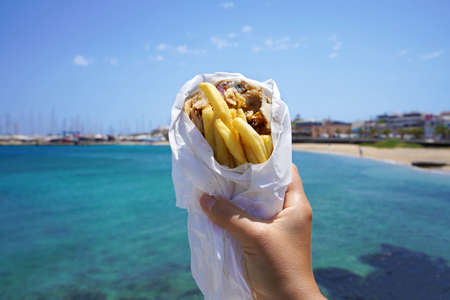 Pita Gyros. Greek gyros wrapped in pita breads against Greek beach with blue sea.の写真素材