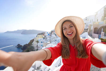 Traveler girl taking selfie photo in Santorini on sunset. Smiling woman having fun in Oia village in Greece.の写真素材