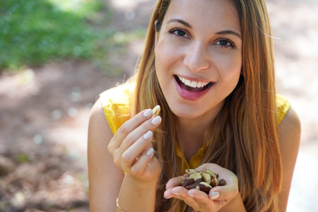 Close-up of healthy woman eating Brazil nuts in the park. Looks at camera.