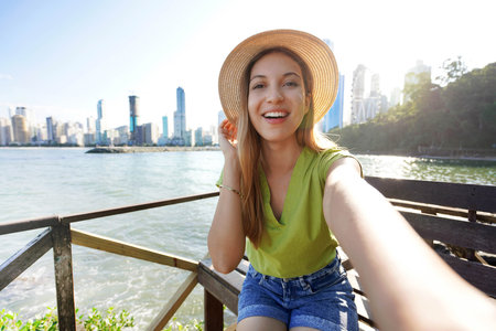 Happy smiling stylish female model takes self portrait with her smartphone in Balneario Camboriu,...
