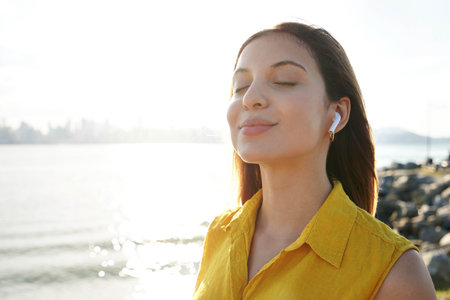 Meditative young woman listening relaxing music with earphones breathing fresh air on sunset